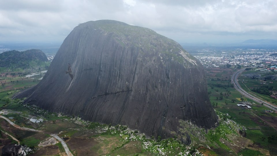 Aerial View of Zuma Rock: Nigeria's Iconic Monolith Dominates a Lush Landscape with Distant City
