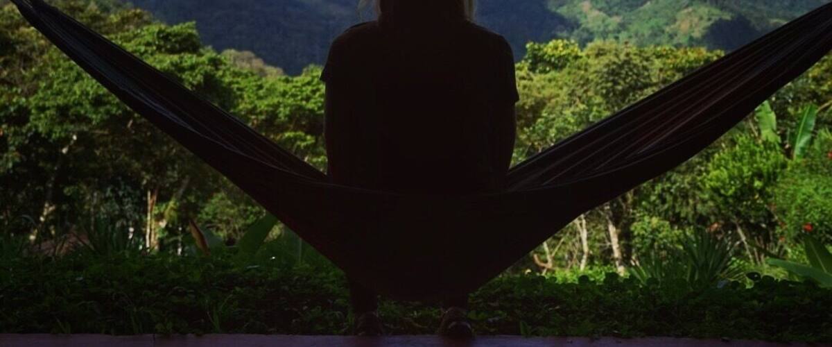 A person sitting in a hammock overlooking a mountainous landscape with a clear sky.