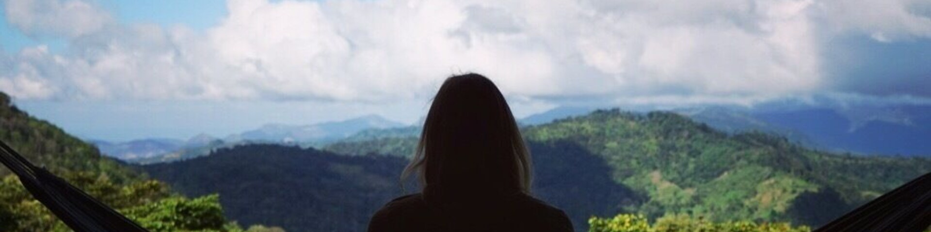 A person sitting in a hammock overlooking a mountainous landscape with a clear sky.