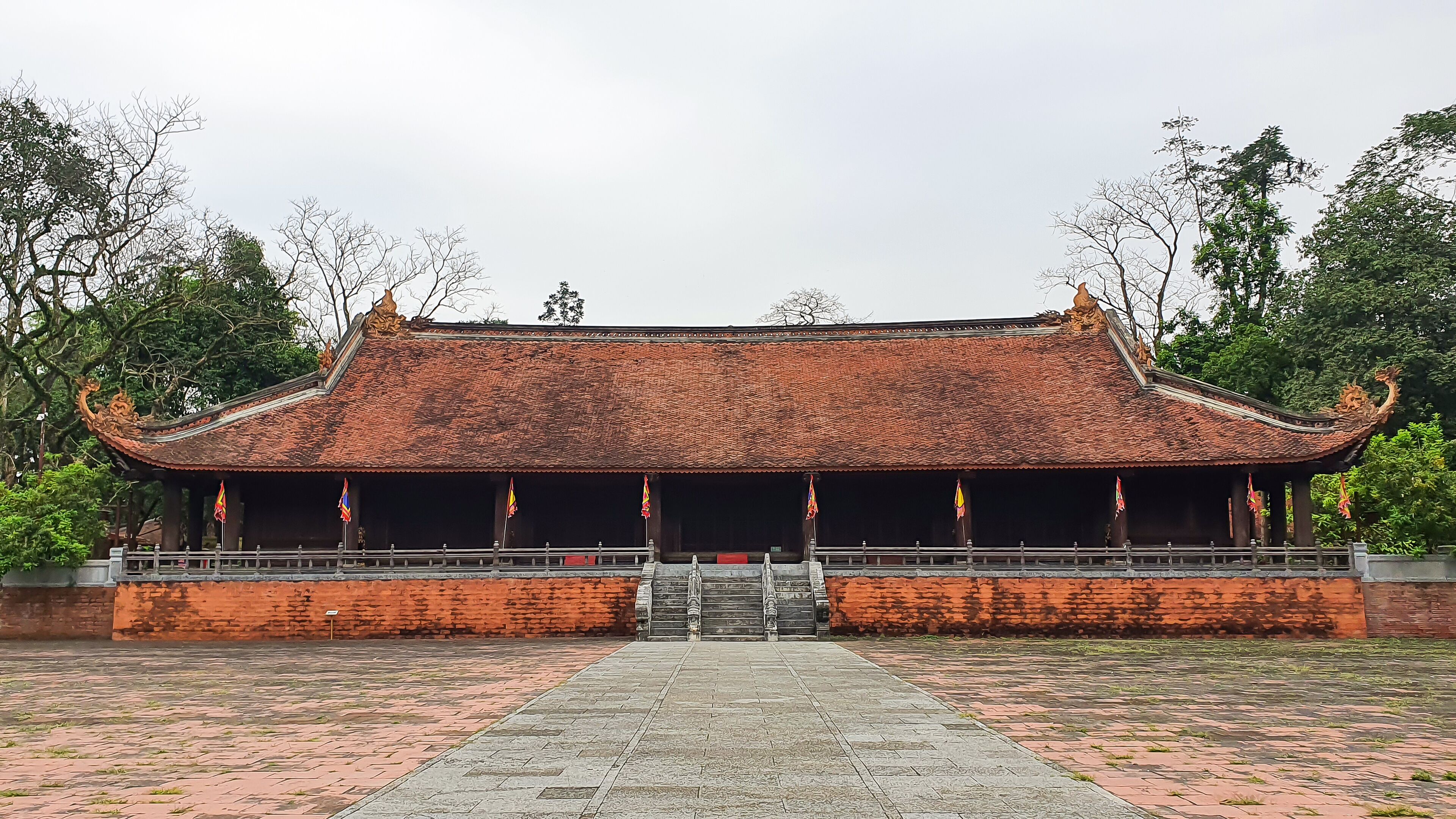 A traditional building with a tiled roof and ornate decorations, surrounded by trees and a paved walkway.