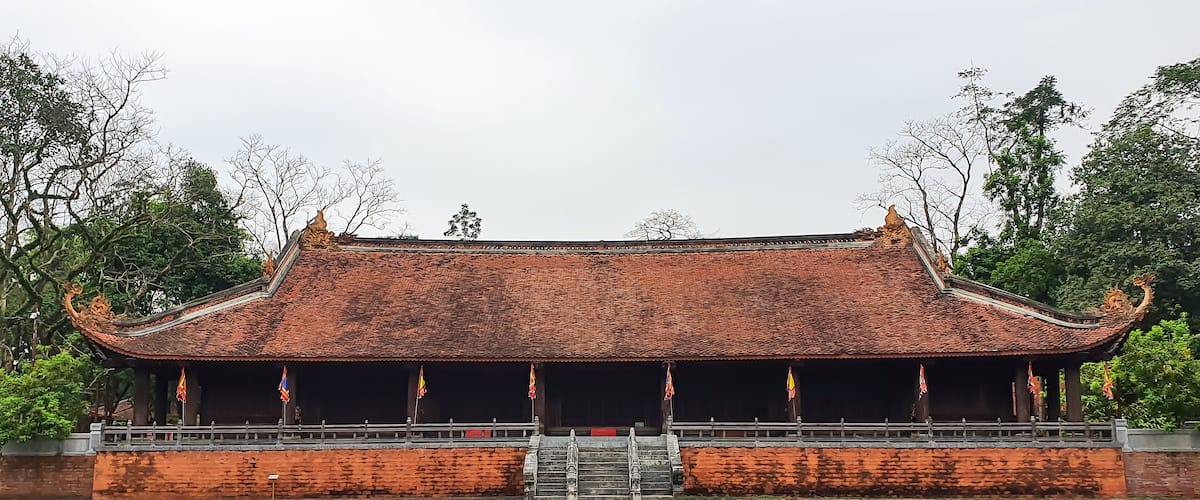 A traditional building with a tiled roof and ornate decorations, surrounded by trees and a paved walkway.