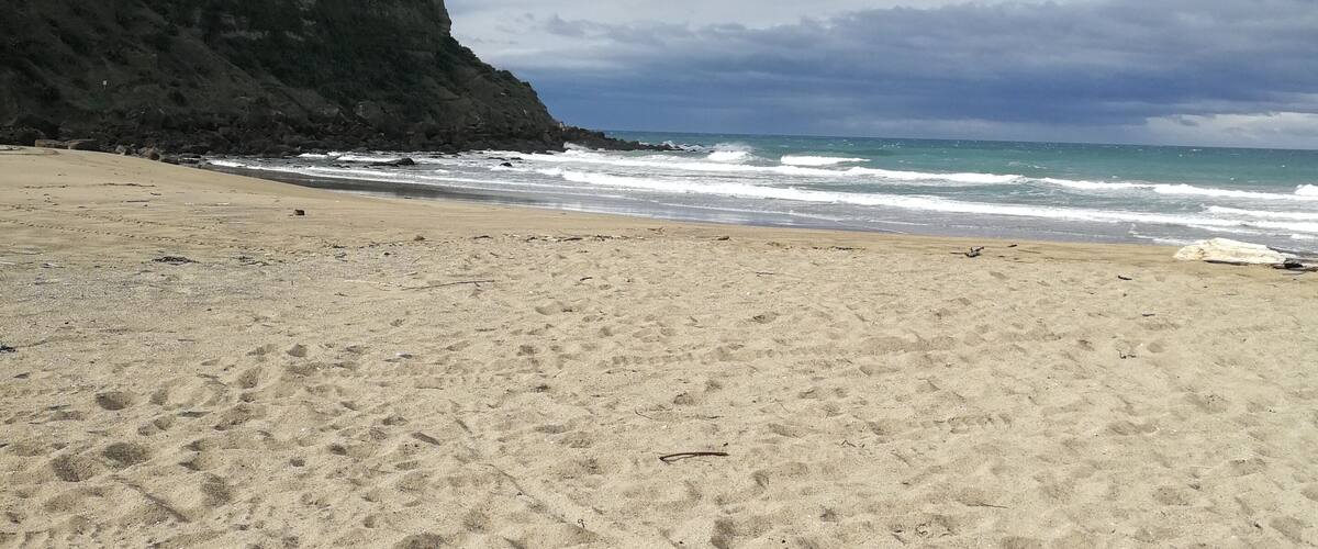 A sandy beach with a large rock in the foreground and a cliff in the background.