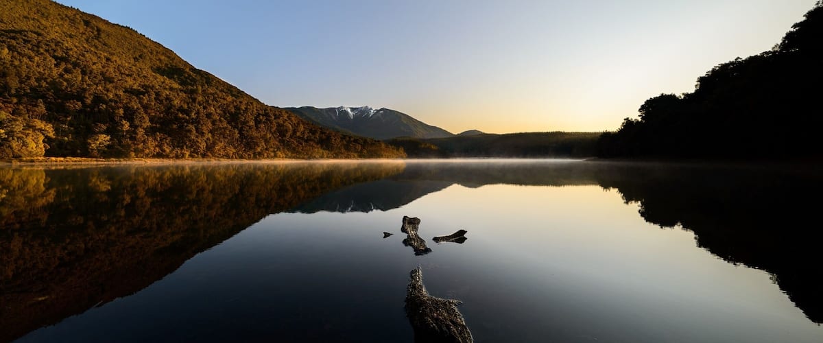 A calm lake with reflections of trees and mountains.