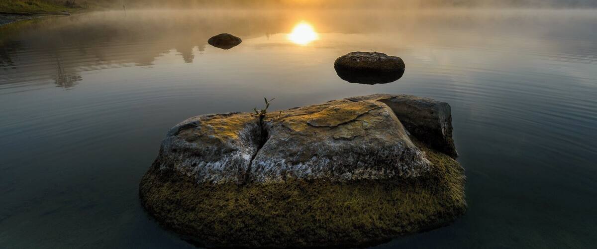 A misty lake with rocks and a sunrise.