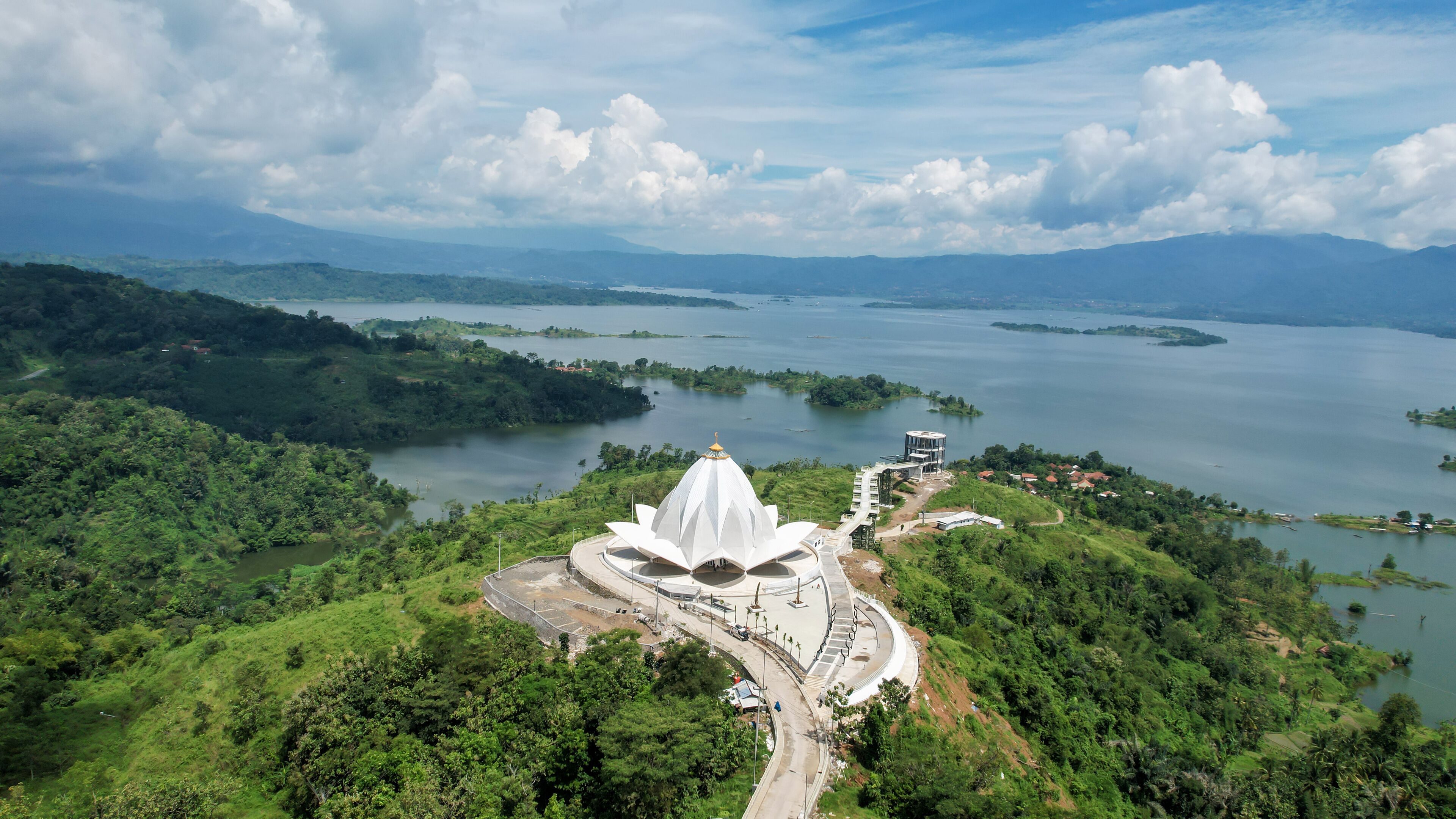 A white lotus-shaped temple surrounded by lush greenery and a large lake.