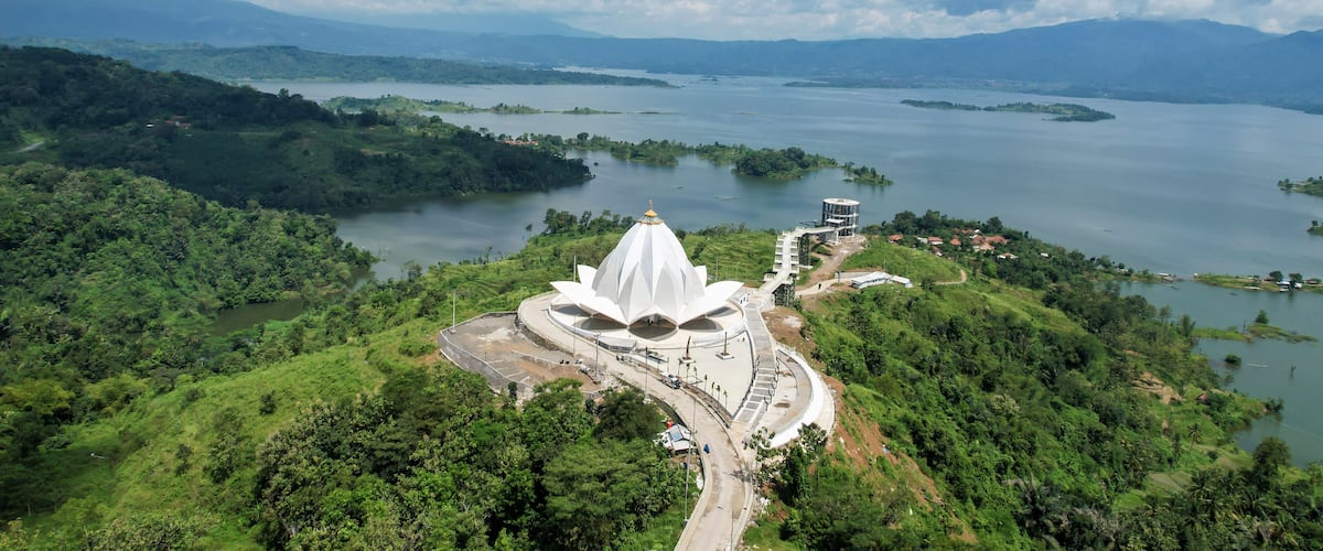 A white lotus-shaped temple surrounded by lush greenery and a large lake.