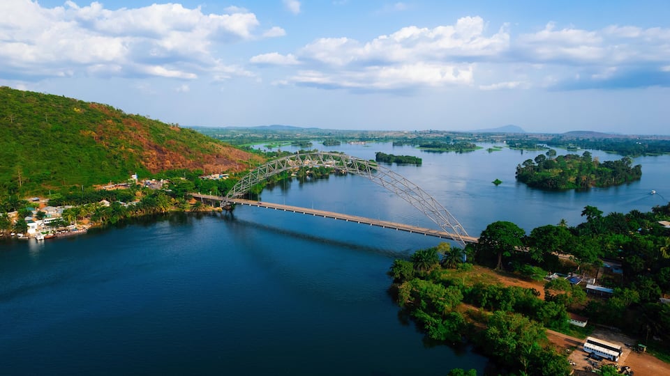 A steel arch bridge over a river with surrounding greenery and hills.