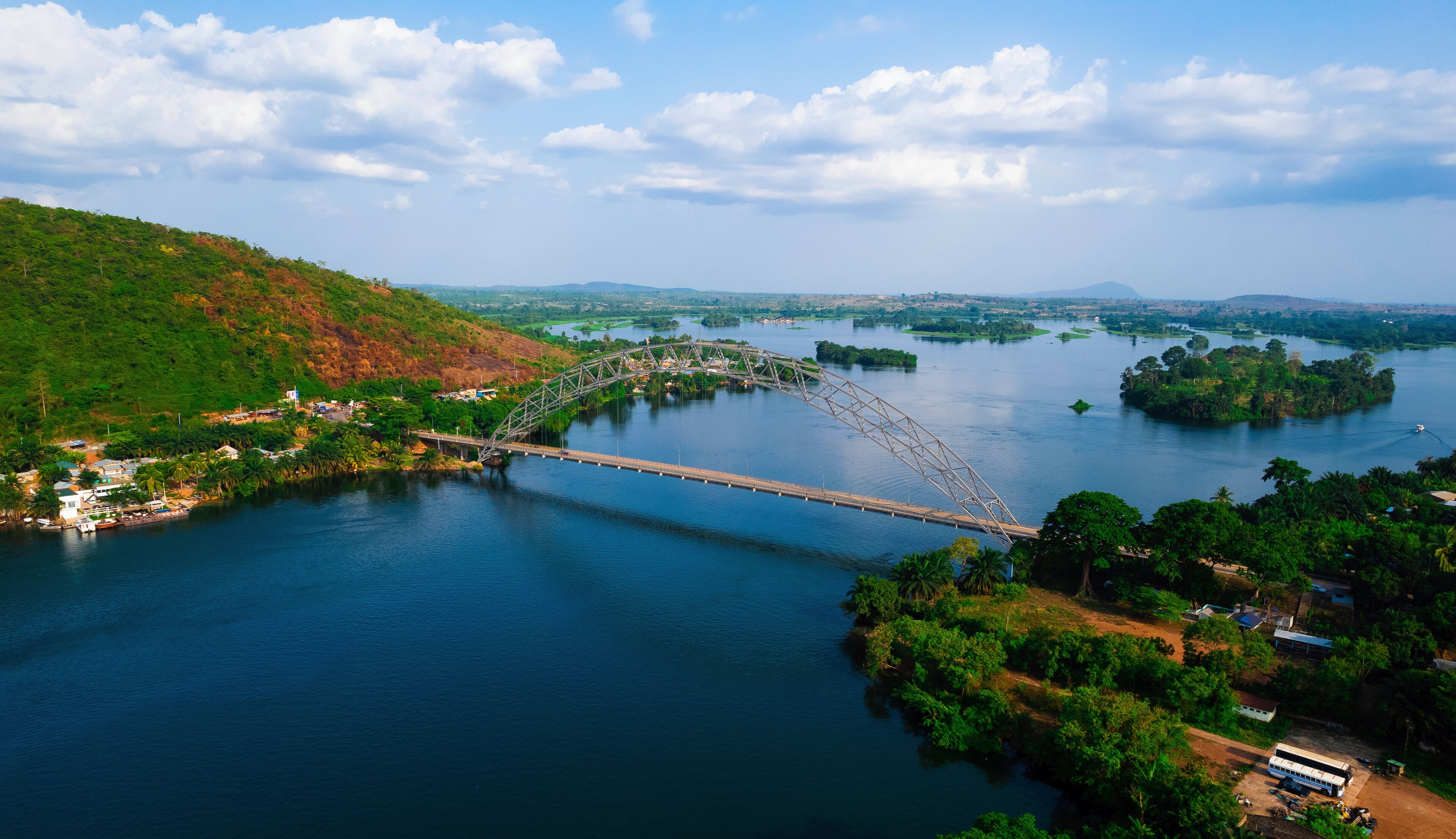 A steel arch bridge over a river with surrounding greenery and hills.