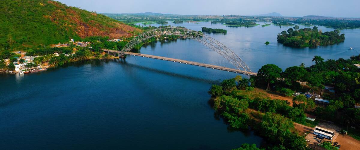 A steel arch bridge over a river with surrounding greenery and hills.