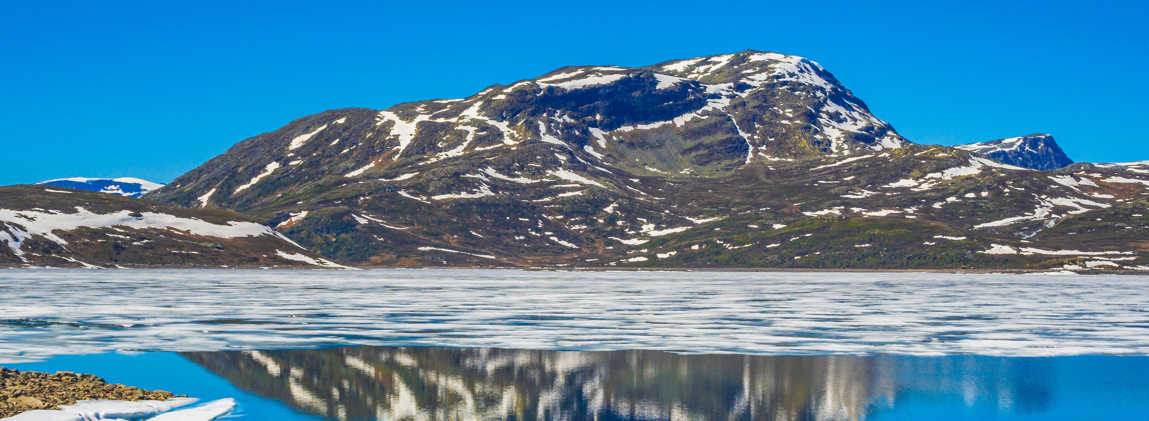 A mountain with snow patches and a calm lake reflecting the mountain.