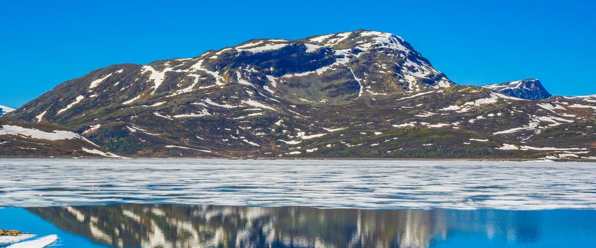A mountain with snow patches and a calm lake reflecting the mountain.