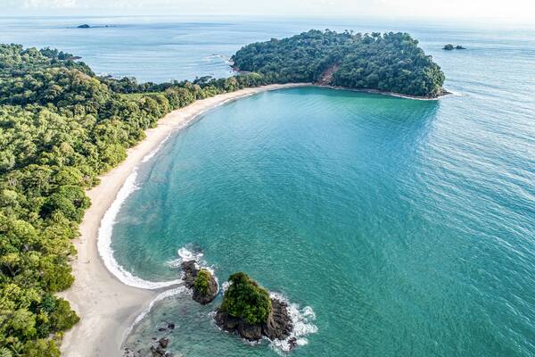Un paisaje costero con una playa arenosa, aguas turquesas cristalinas y una isla verde exuberante.