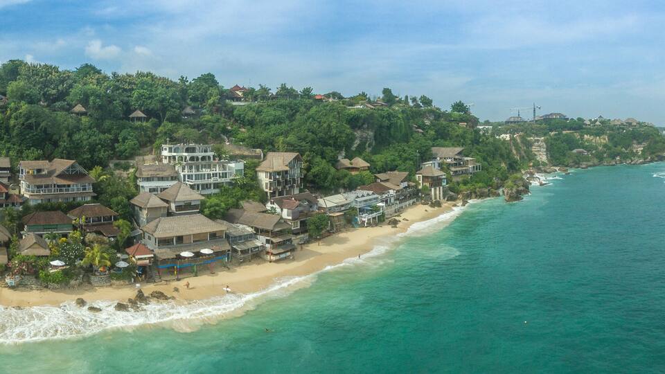A coastal town with a beach, houses, and a forested hillside.