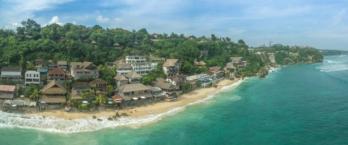 A coastal town with a beach, houses, and a forested hillside.