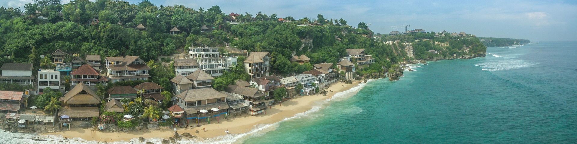 A coastal town with a beach, houses, and a forested hillside.