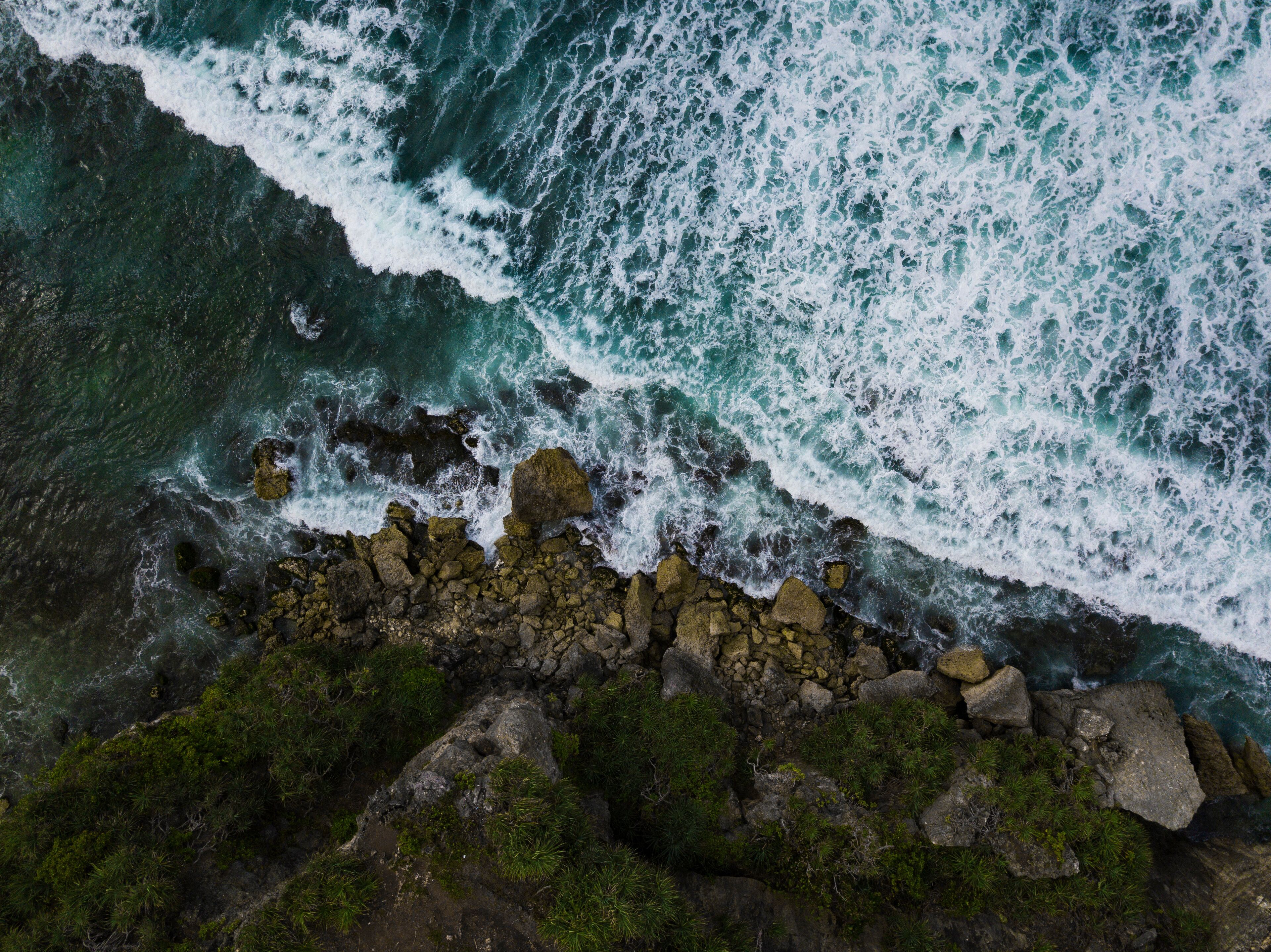 Overhead view of The bluish ocean waves crashing against the rocks on the beach produce white ripples and foam in tropical beach