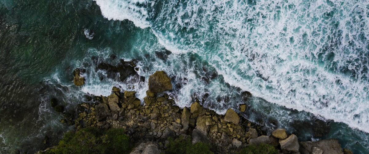 Overhead view of The bluish ocean waves crashing against the rocks on the beach produce white ripples and foam in tropical beach