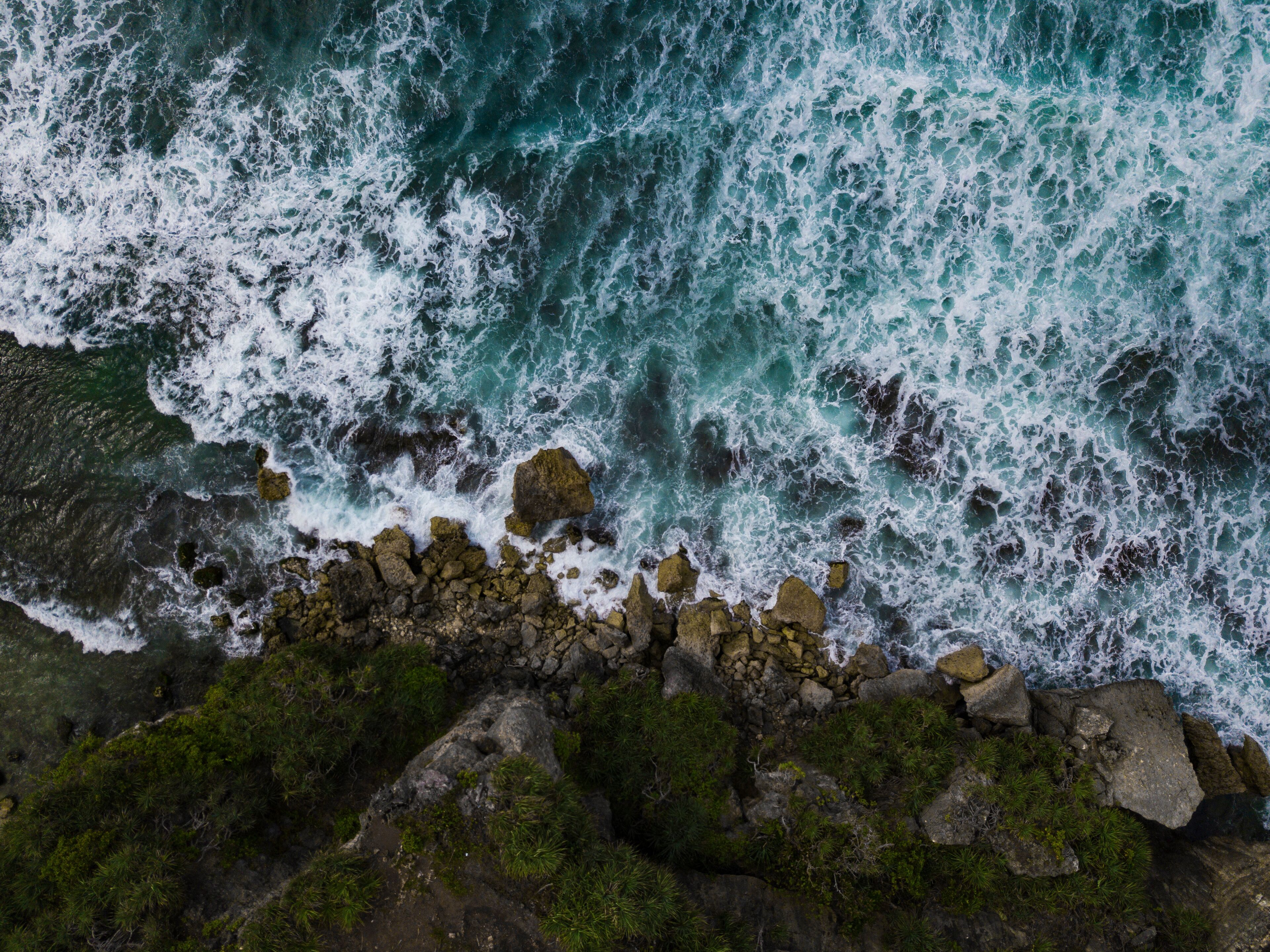 Overhead view of The bluish ocean waves crashing against the rocks on the beach produce white ripples and foam in tropical beach