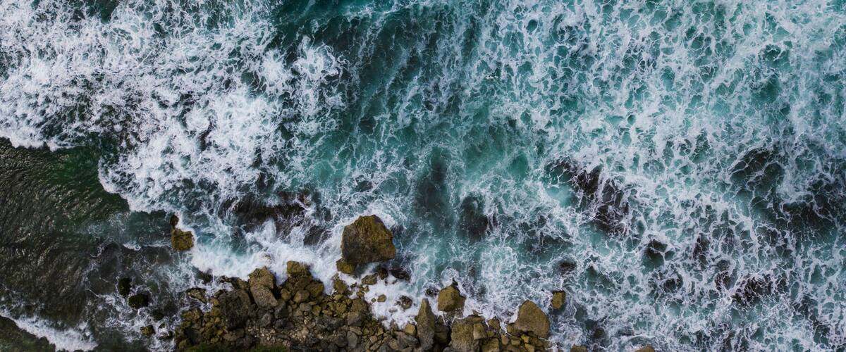 Overhead view of The bluish ocean waves crashing against the rocks on the beach produce white ripples and foam in tropical beach