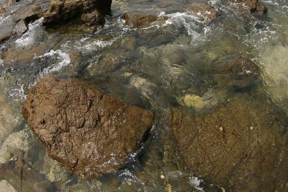 Uma linha costeira rochosa com água límpida e ondas batendo nas pedras.