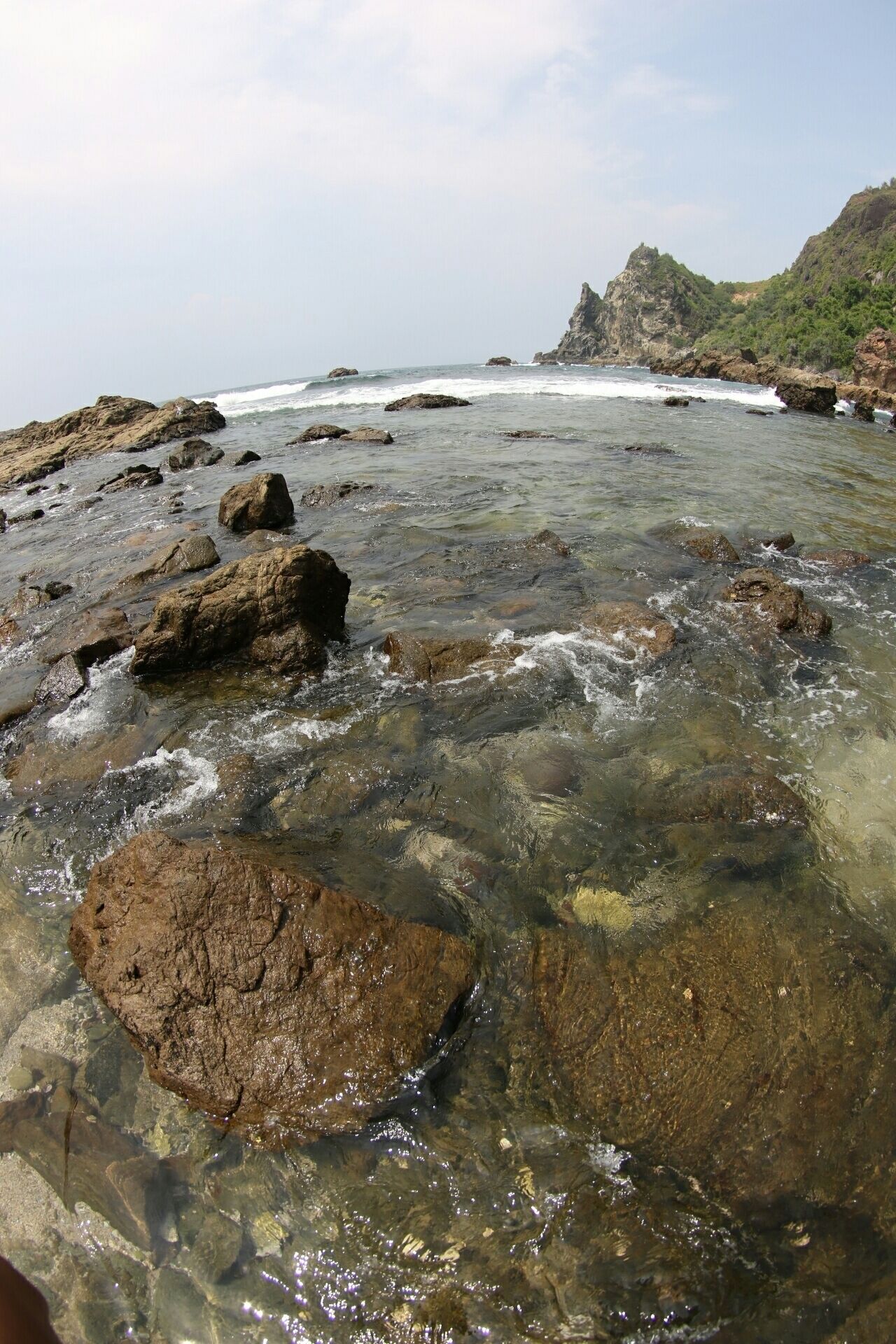 A rocky shoreline with clear water and waves crashing against the rocks.