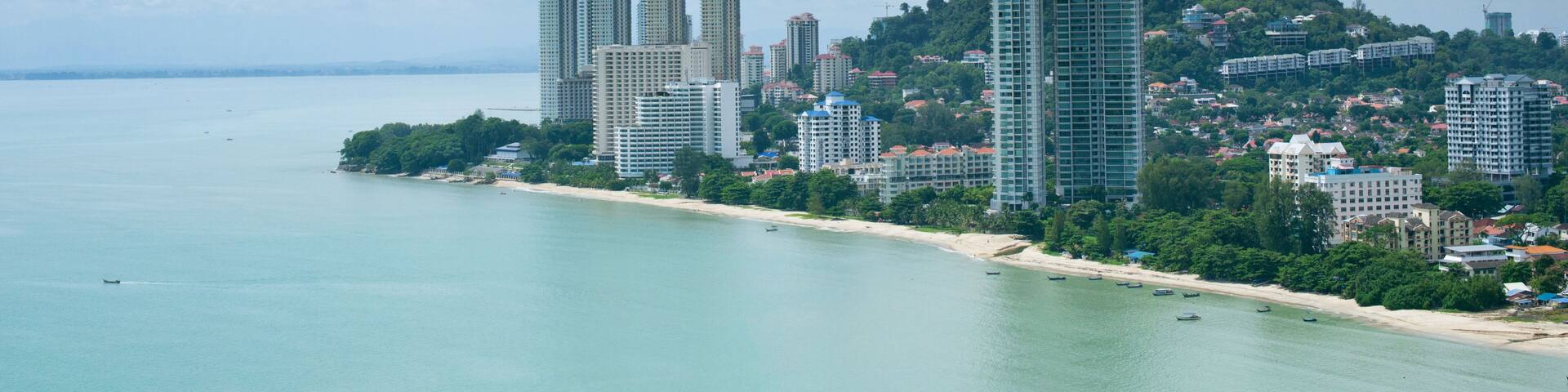 A coastal cityscape with high-rise buildings, a beach, and a hill with greenery.