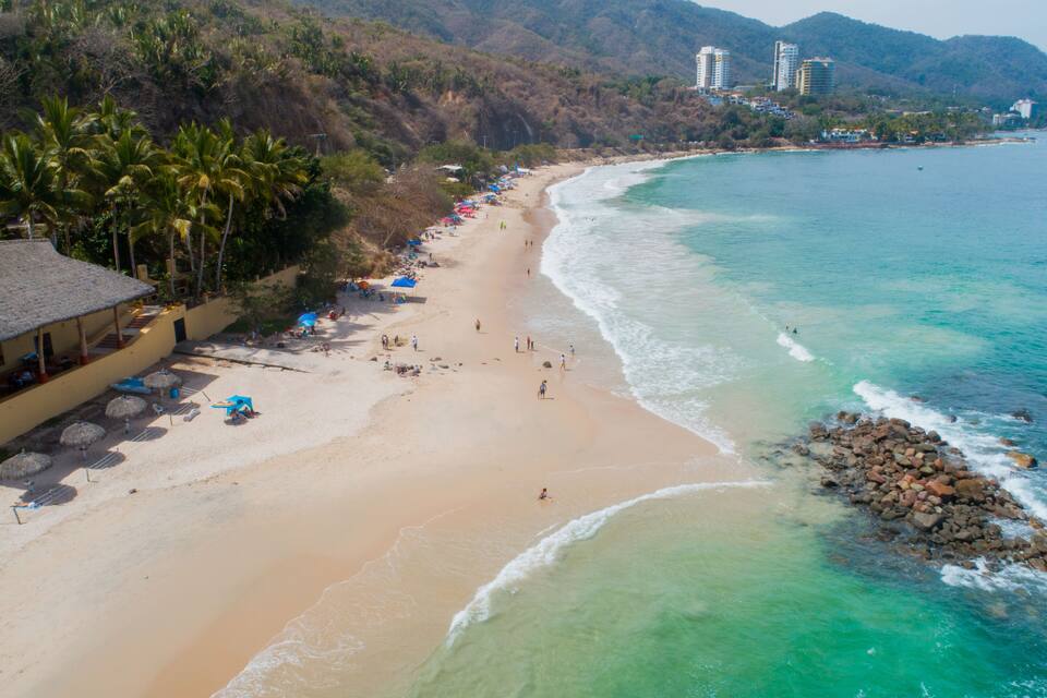 A beach with clear turquoise waters, a sandy shore, and palm trees.