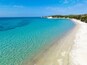 Ein klares türkisblaues Meer, ein weißer Sandstrand und ein bewaldeter Hügel in der Ferne.