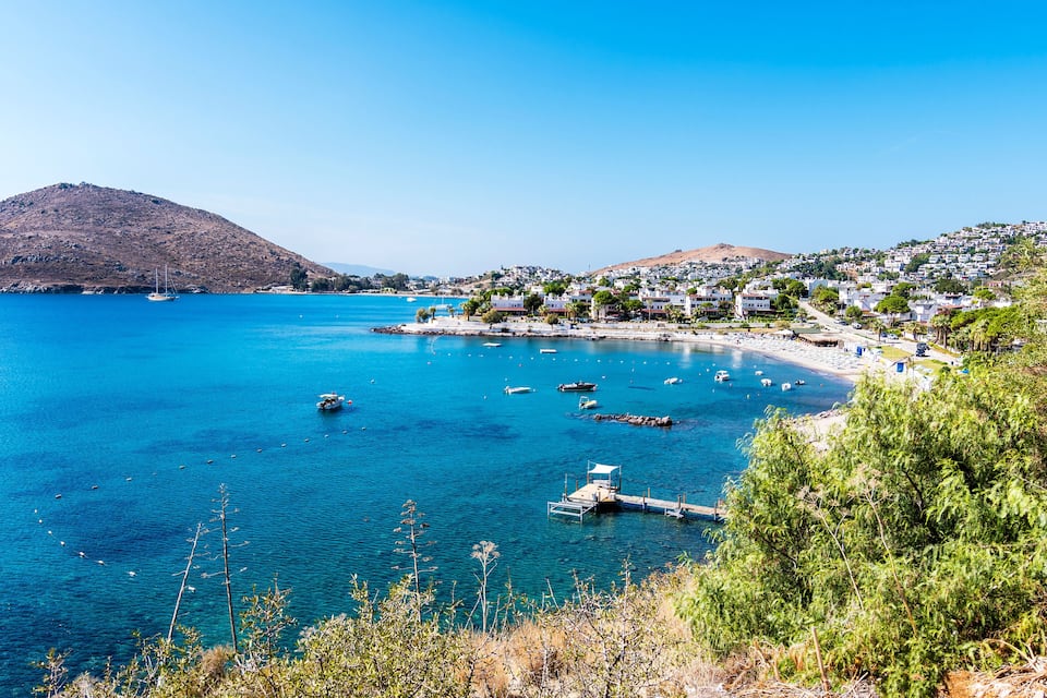 A coastal town with clear blue waters, boats, and a hilly backdrop.