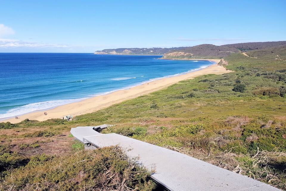 A coastal landscape with a beach, ocean, and hilly terrain.