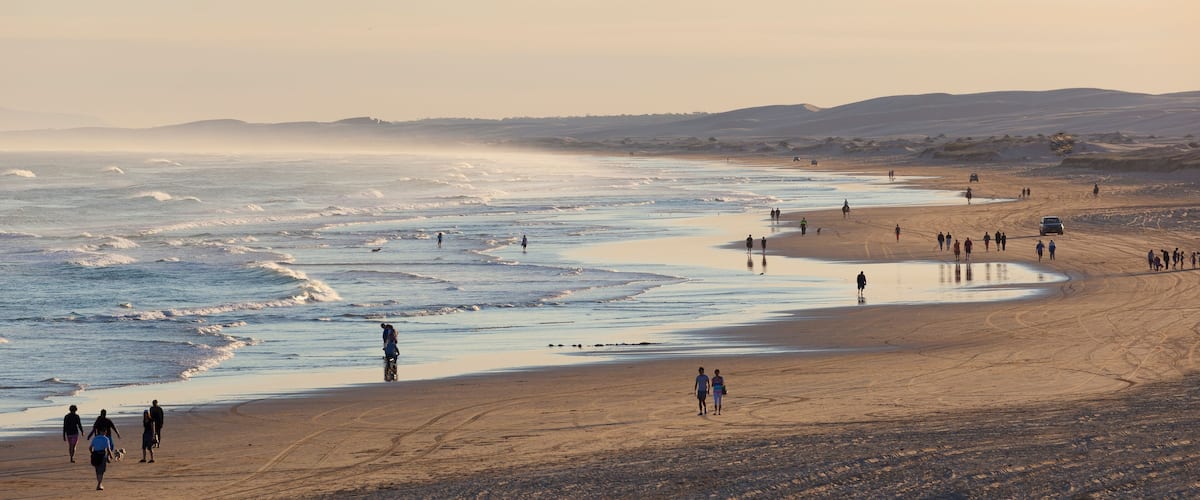 A beach with people walking and horseback riders.