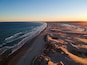 Eine Küstenlandschaft mit Sandstrand und Wellen im Sonnenuntergang.