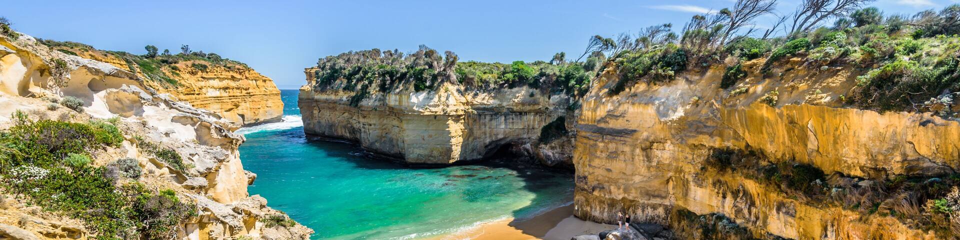 Un paisaje costero con una playa arenosa, acantilados rocosos y aguas azul cristalino.