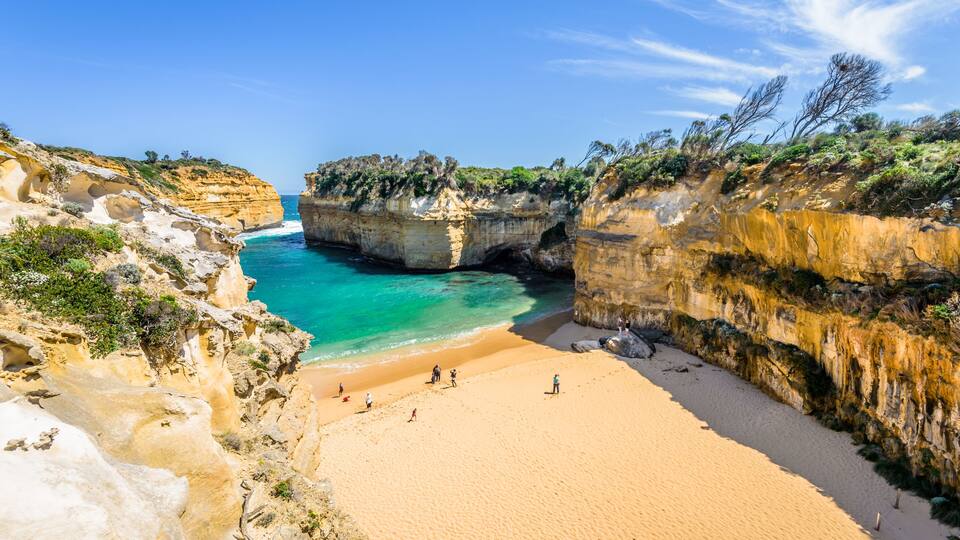 A coastal landscape with a sandy beach, rocky cliffs, and clear blue waters.