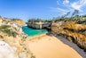 A coastal landscape with a sandy beach, rocky cliffs, and clear blue waters.