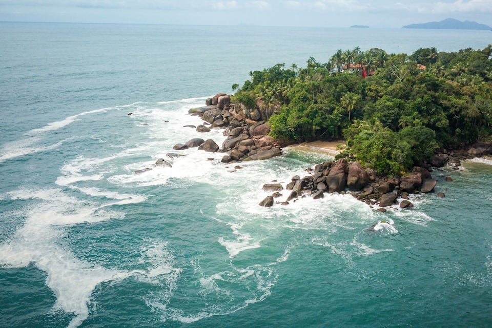 Paisagem costeira com costas rochosas, vegetação verde densa e uma vista clara do oceano.