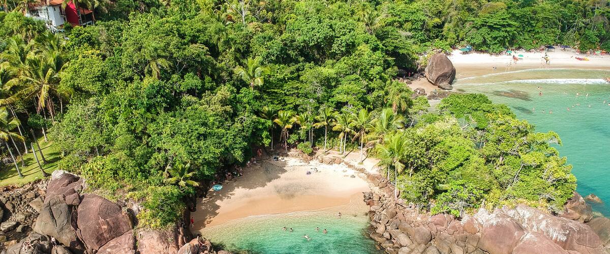 A tropical beach with clear turquoise waters, surrounded by dense green foliage and large rocks.