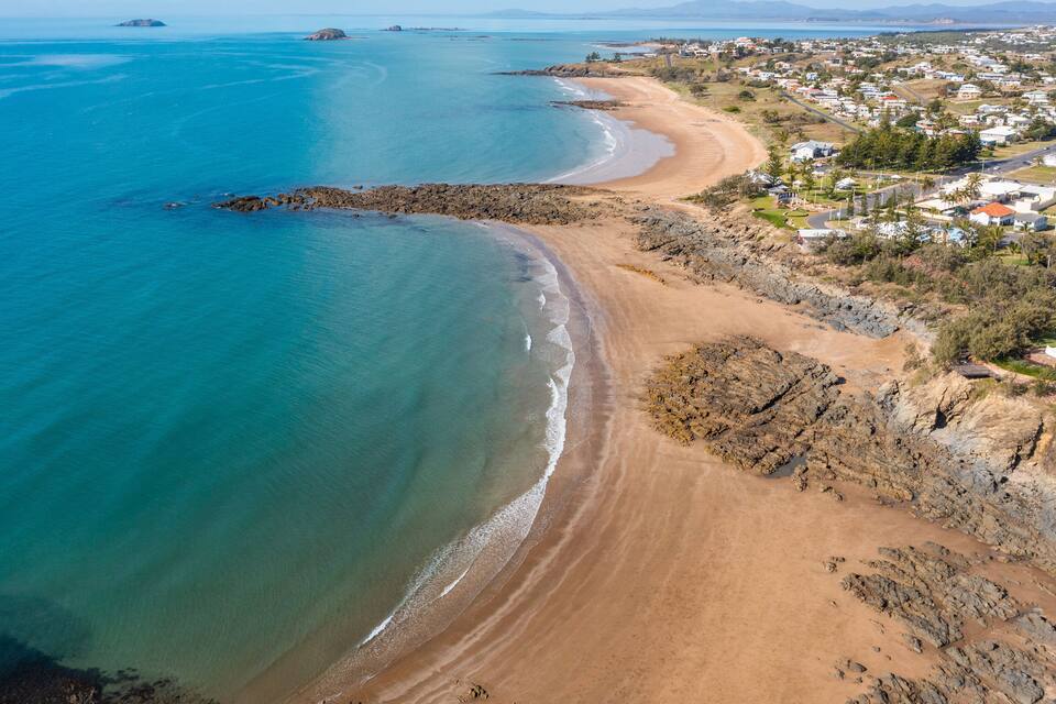 A coastal town with a sandy beach, rocky shoreline, and residential buildings.