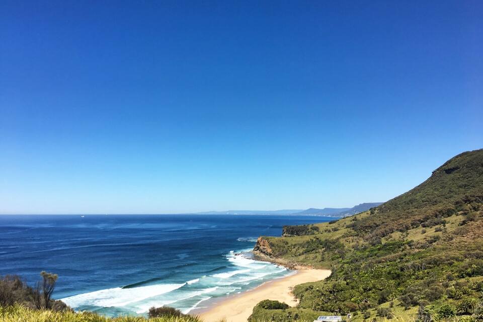 Eine Küstenlandschaft mit Strand, Meereswellen und grünen Hügeln.
