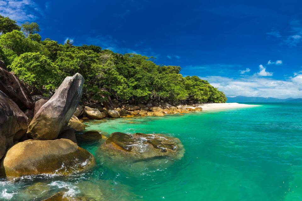 Ein türkisfarbener Strand mit großen Felsen und dichtem, grünem Grün.