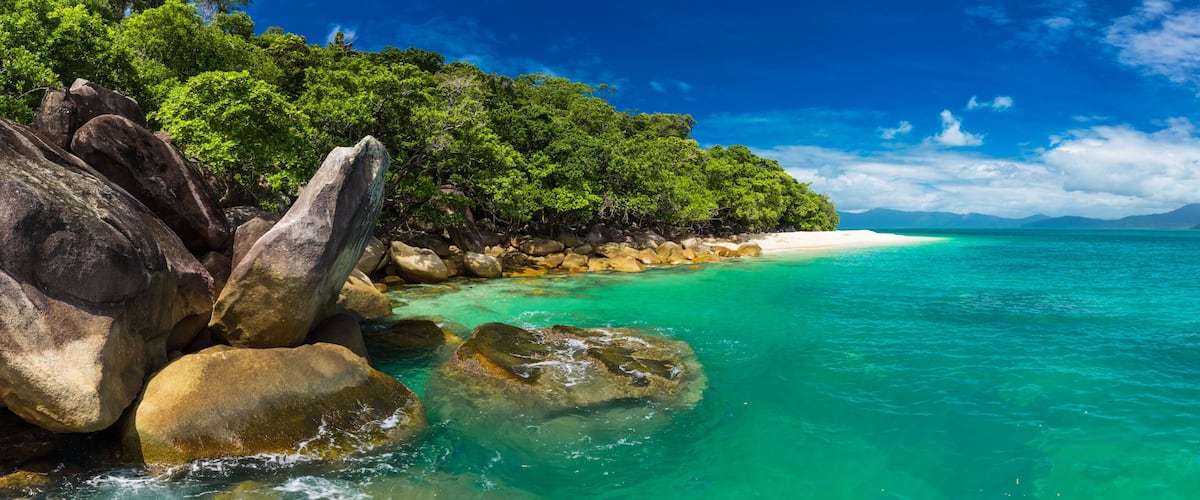 A turquoise beach with large rocks and dense green foliage.