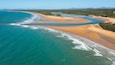 Un paysage côtier caractérisé par une plage de sable, des eaux turquoise et une rivière qui serpente à travers le terrain.