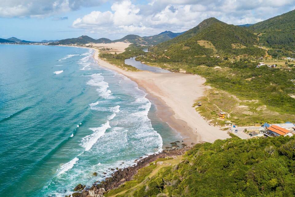 Un paisaje costero con una playa arenosa, un río sinuoso y colinas verdes exuberantes.