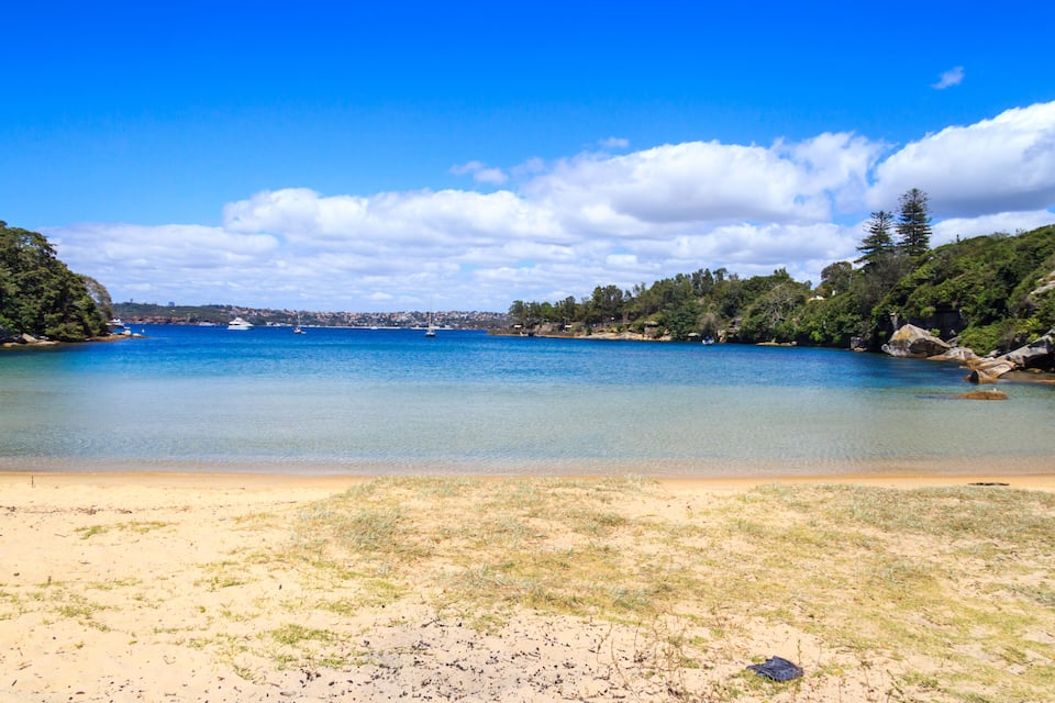 Una platja costanera amb aigua blau clar, sorra daurada i vegetació al voltant.