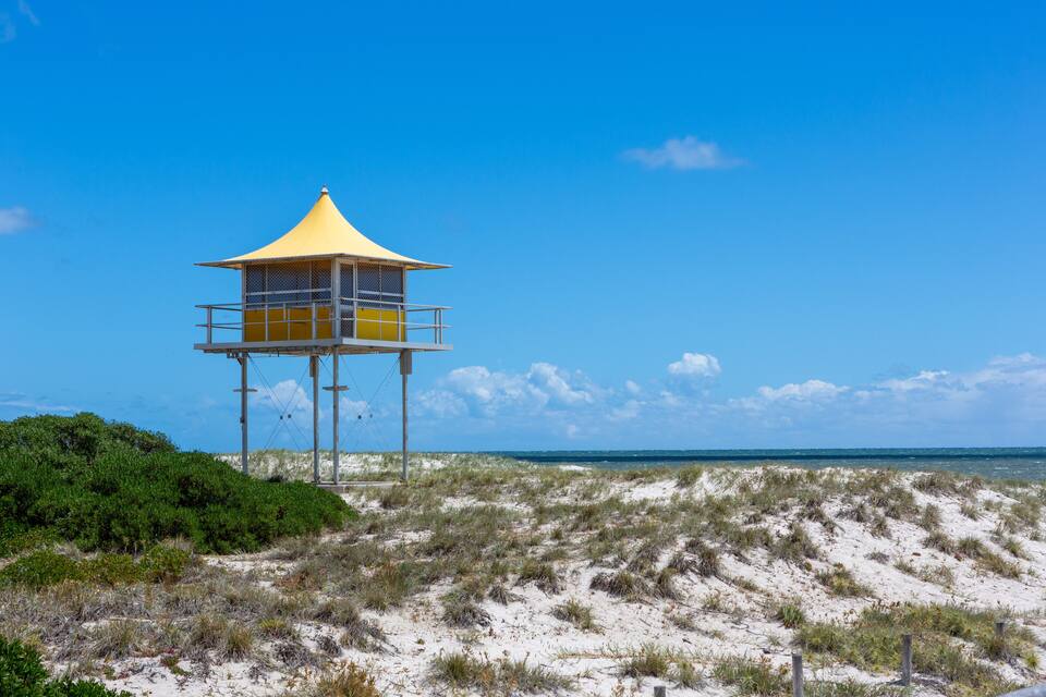 A beach lookout tower with a yellow roof, surrounded by sand dunes and sparse vegetation.