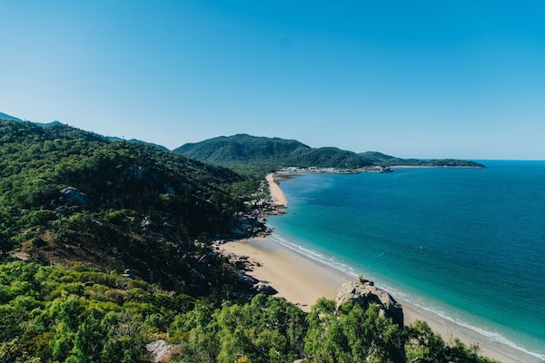 Eine Küstenlandschaft mit sandigem Strand, dichtem Grünwald und klarem, blauem Meer.