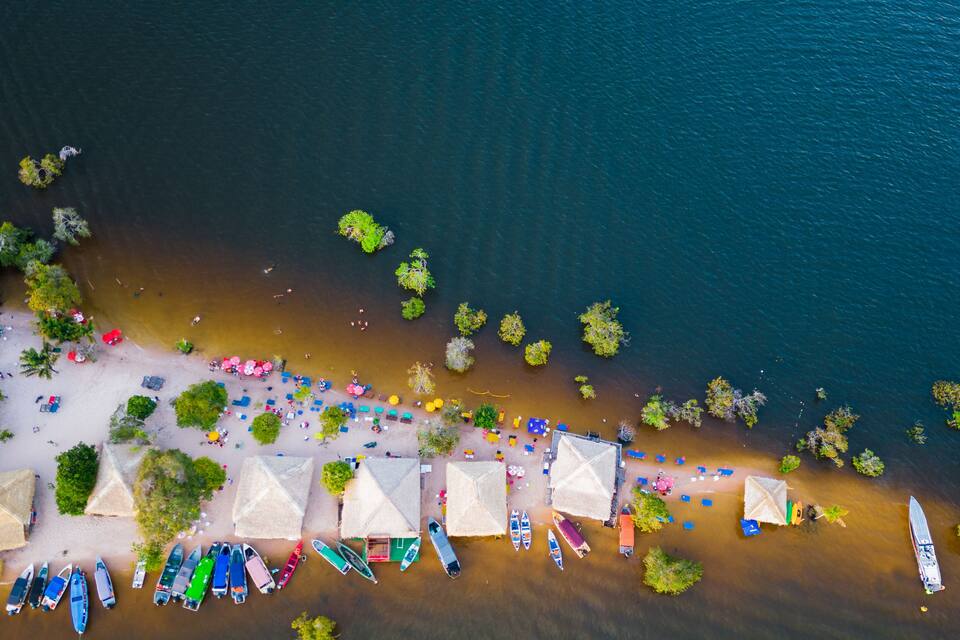 An aerial view of a beach with boats, umbrellas, and thatched-roof huts.
