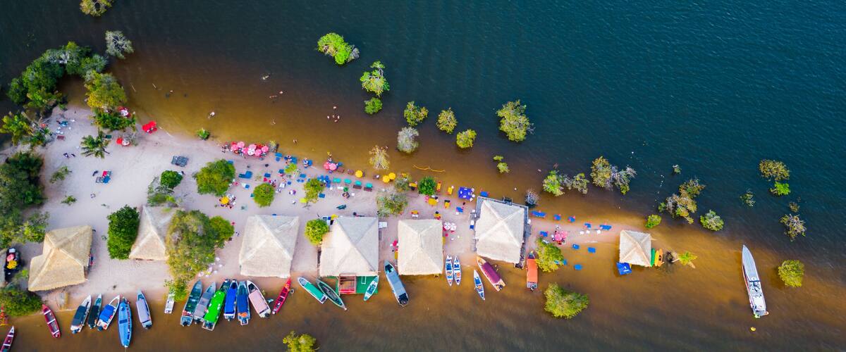 An aerial view of a beach with boats, umbrellas, and thatched-roof huts.