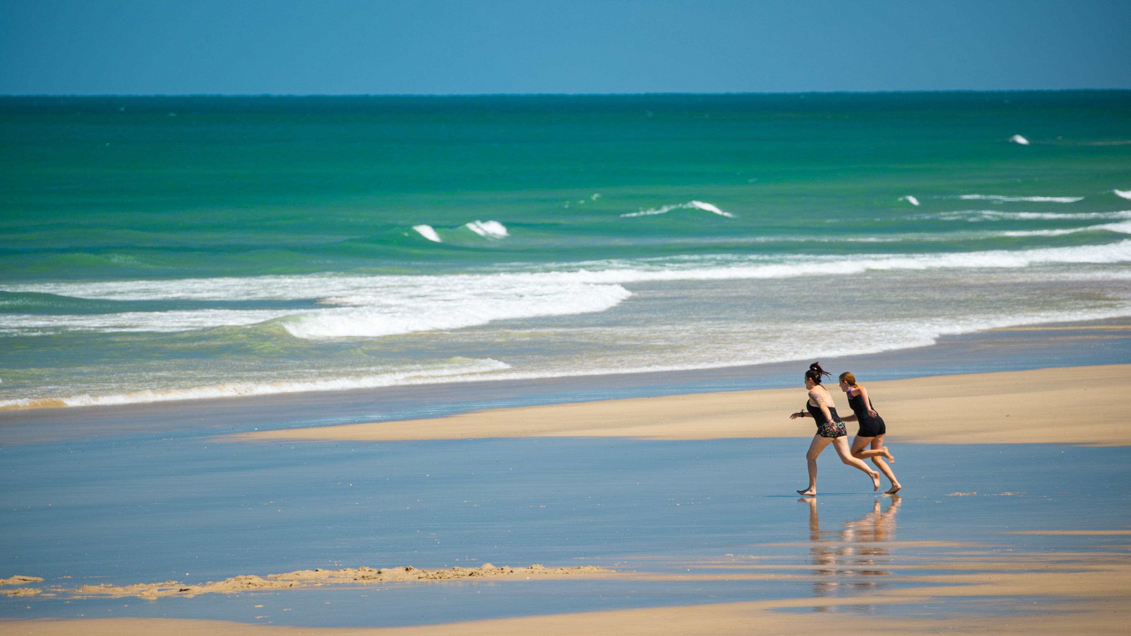 A beach with waves and two people running.