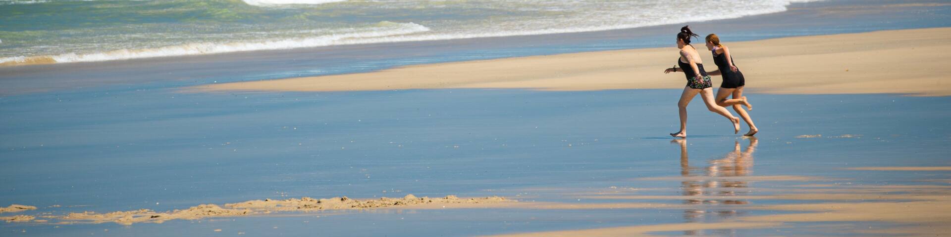 A beach with waves and two people running.